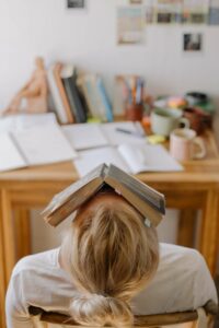 Frau nach hinten gelehnt mit Buch auf ihrem Gesicht, die vor einem Schreibtisch sitzt